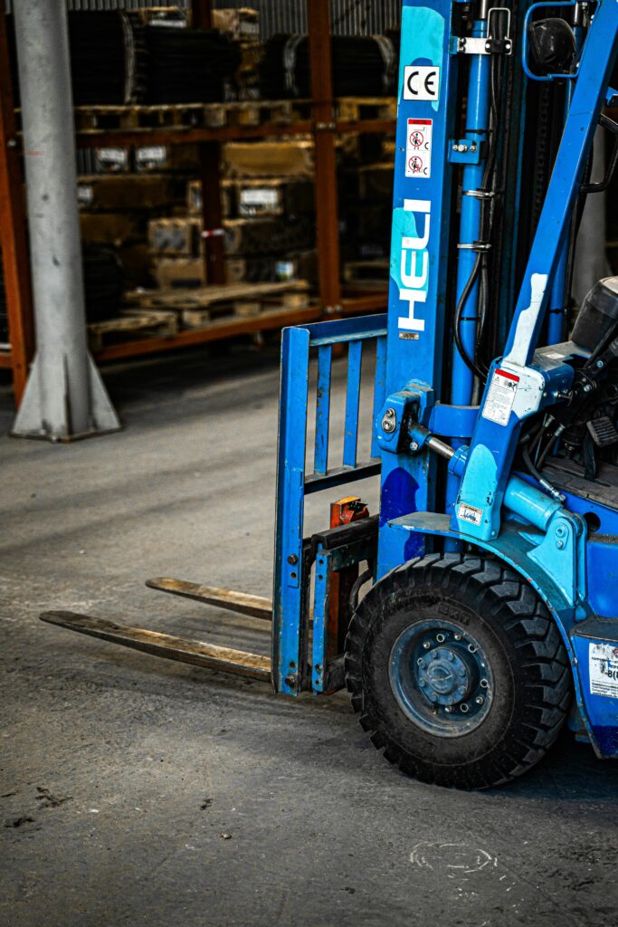 Blue forklift inside an industrial warehouse, parked near shelves with various items.